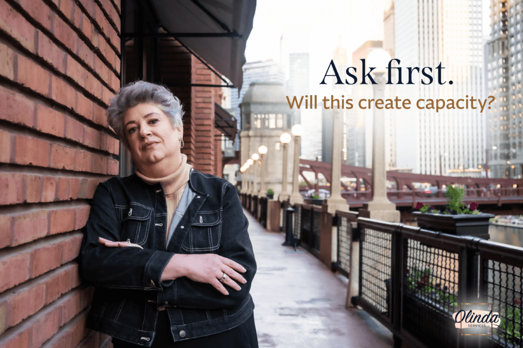 Lisa Olinda beside a brick wall overlooking a city riverwalk. Text reads, “Ask first. Will this create capacity?